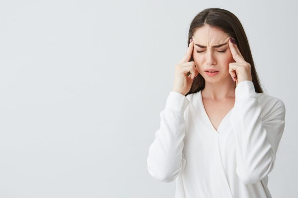Young beautiful brunette businesswoman holding fingers on temples frowning from pain over white background. Headache. Copy space.